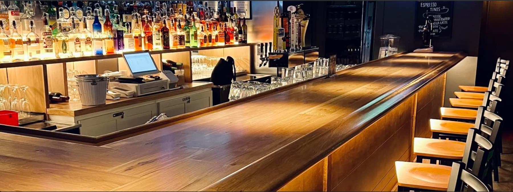 The long polished wood bar at Beaufort Bar, back bar fully stocked, stools ready
